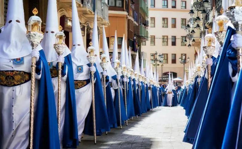 На изображении, люди одеты в религиозные костюмы с высокими колпаками на головах, Фестиваль в Испании 